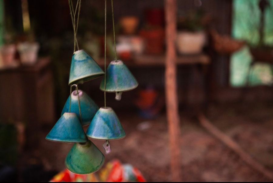 Verdigris ceramic wind chimes hanging in a shadowed potting shed