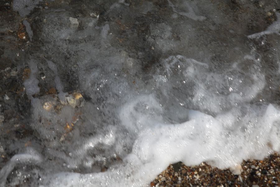 White sea foam laces across wet pebbles and shell-flecked sand
