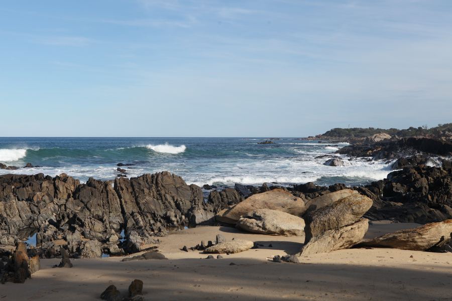 Morning light on a rocky cove, surf rolling toward sandy shallows